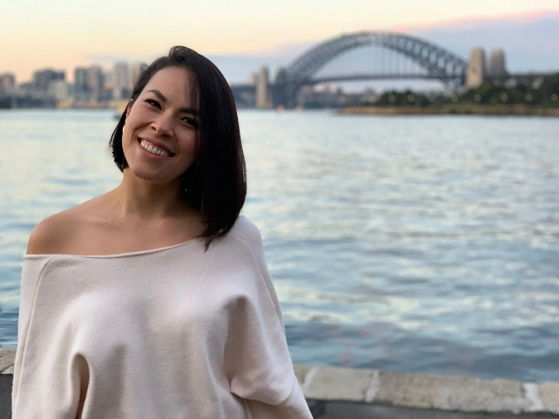 Carolina sonriendo frente al Puente de la Bahía de Sídney al atardecer