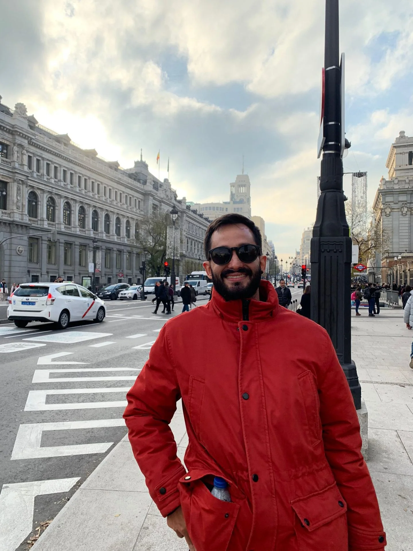 Nacho sonriendo con chaqueta roja en una calle soleada de Madrid